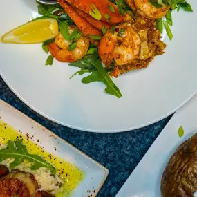 An assortment of seafood dishes served at Slacks Oyster House, including seared scallops, shrimp on a bed of greens, and a baked potato. Each dish is meticulously plated, showcasing the restaurant's dedication to fresh, high-quality ingredients.