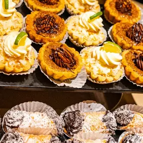 n elegant dessert display at Slacks Oyster House, showcasing a variety of mini tarts, cannolis, and cream-topped treats. The selection includes pecan tarts, coconut cream tarts, and chocolate-filled pastries, all beautifully arranged for a sweet finale to your meal.