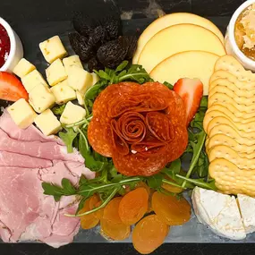 A gourmet charcuterie board at Slacks Oyster House, Plainridge Park Casino, featuring an array of sliced meats, cheeses, crackers, and fresh fruits. The board includes pepperoni arranged in a rose shape, smoked gouda, cubes of sharp cheddar, and a variety of crackers, all artfully presented.