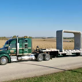 A Morrell Transfer semitruck is driving down a country road, hauling a large, rectangular concrete structure on its flatbed trailer.