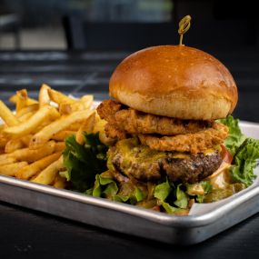 Our Hatch Green Chile Queso Burger, with lettuce, tomato, a generous helping of our queso, hatch green chiles, and four onion rings.