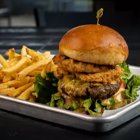 Our Hatch Green Chile Queso Burger, with lettuce, tomato, a generous helping of our queso, hatch green chiles, and four onion rings.