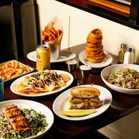 table filled with food: salad, patty melt, grilled salmon, fries, sweet potato fries