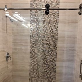 The glass #shower door in this recent guest bathroom #remodeling project features ladder pull handles and a roller system, all with a chrome finish.
